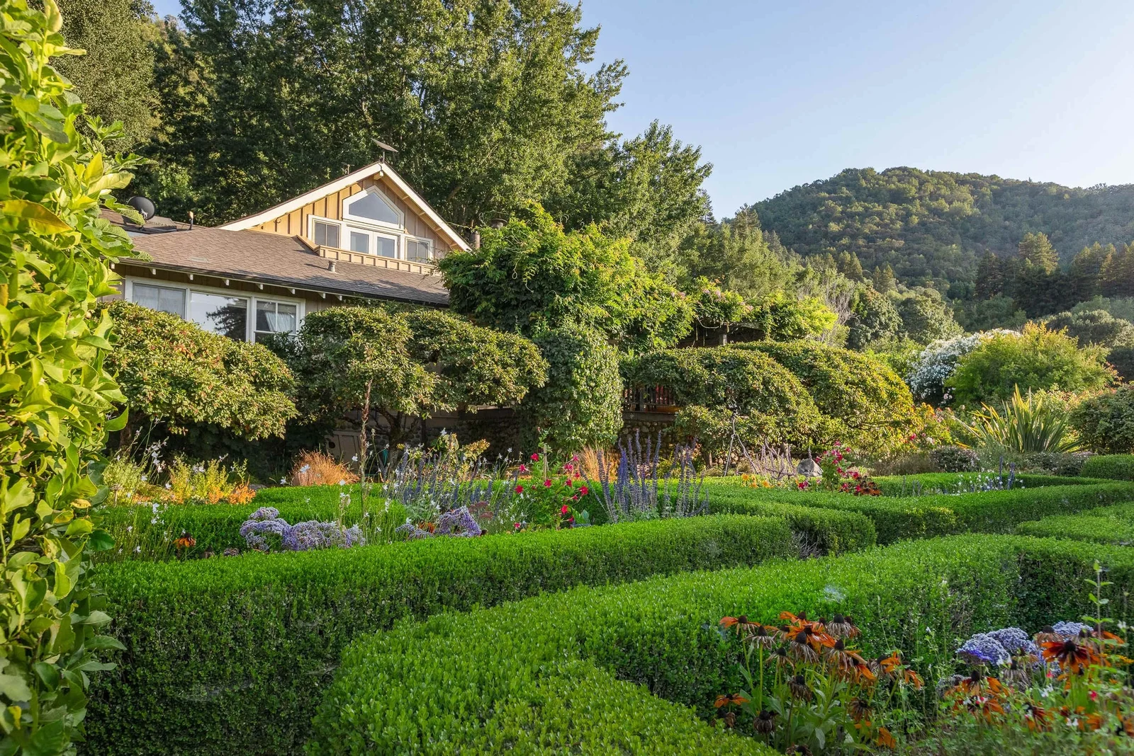 Sonoma Sanctuary house surrounded by clipped hedges, flowering gardens, and wooded hills.