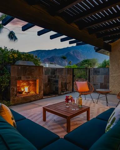 Outdoor lounge with stone fireplace, teal sofas, and mountain views at sunset