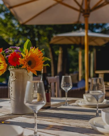 Outdoor dining table set with wine, sunflowers, and glassware on a sunny afternoon