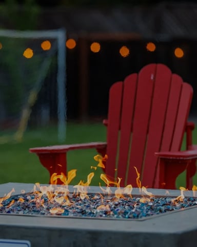Red Adirondack chair beside a lit fire pit in a backyard with string lights at dusk