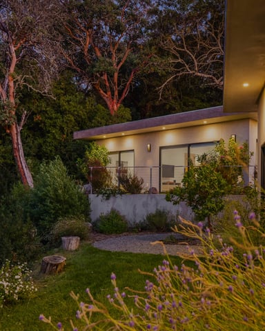 Modern flat-roof house exterior at dusk surrounded by lavender, wildflowers, and lit garden