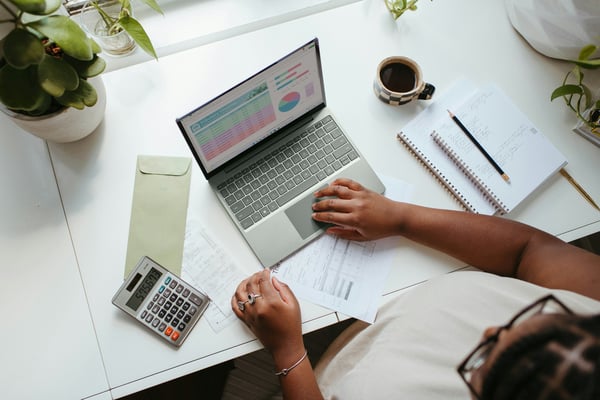 Person reviewing financial reports at a desk with a laptop showing a dashboard and a calculator