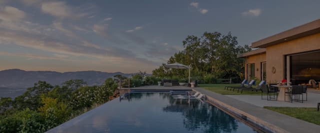 Infinity pool overlooking rolling hills and valleys, with patio seating and loungers on manicured lawn