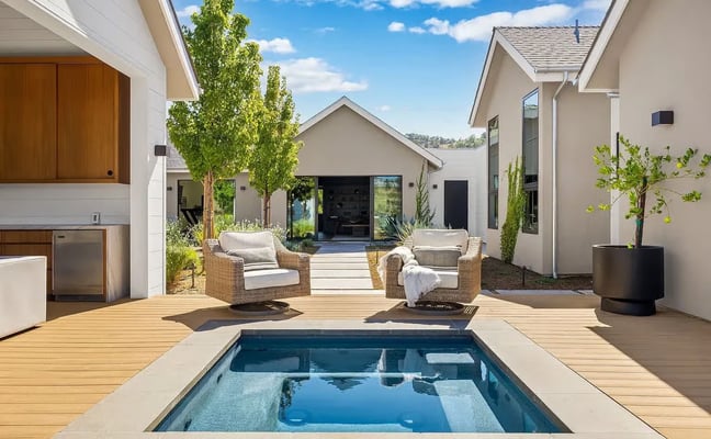 Infinity pool overlooking rolling hills and valleys, with patio seating and lounge chairs on manicured lawn