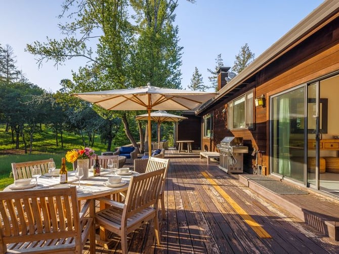 Modern white house with metal roof, wooden front door, and driveway surrounded by mature trees and landscaping